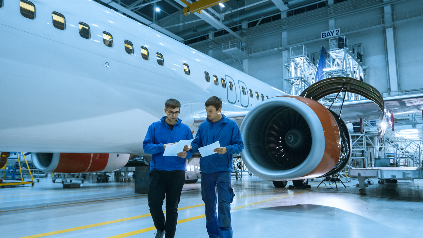 Aircraft maintenance mechanics talk in front of a airplane cabin in a hangar.