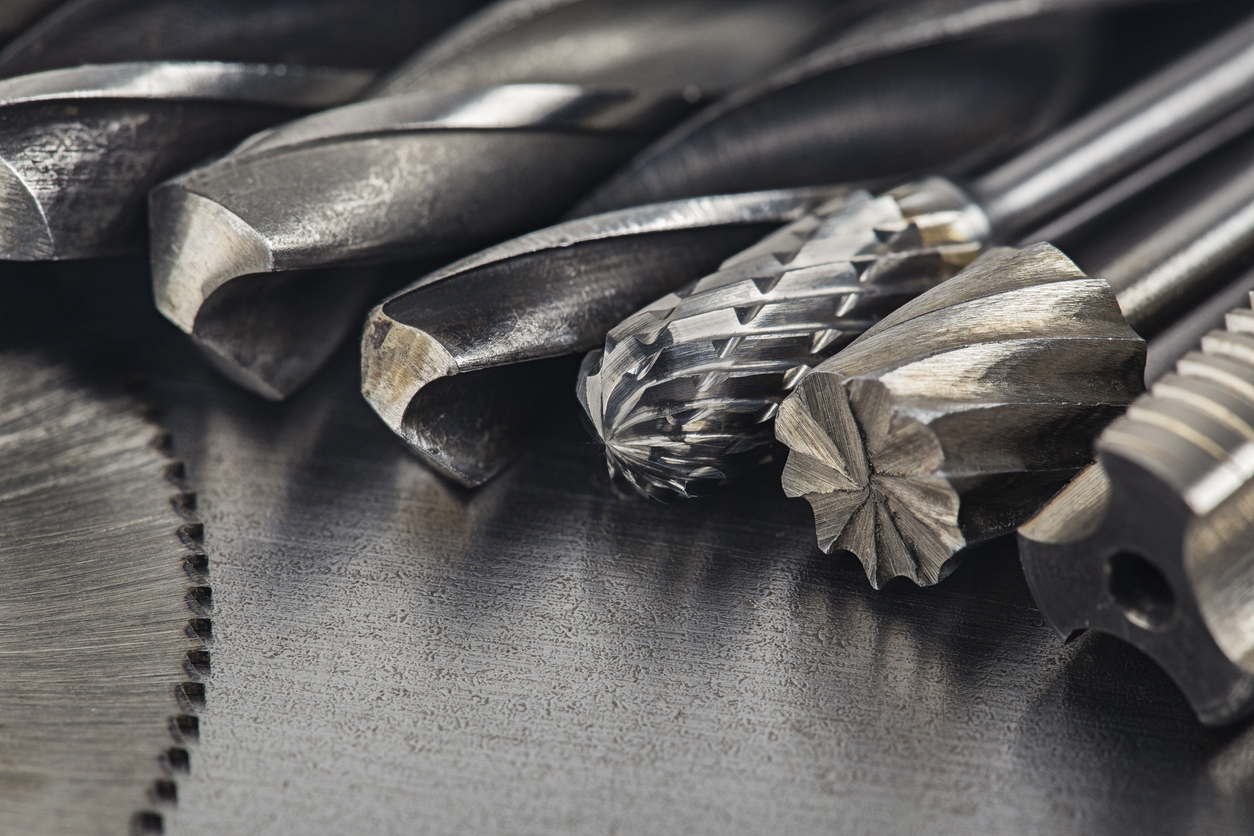 set of different drill bits, thread tap and mill cutters with caliper ruler on steel plate background.