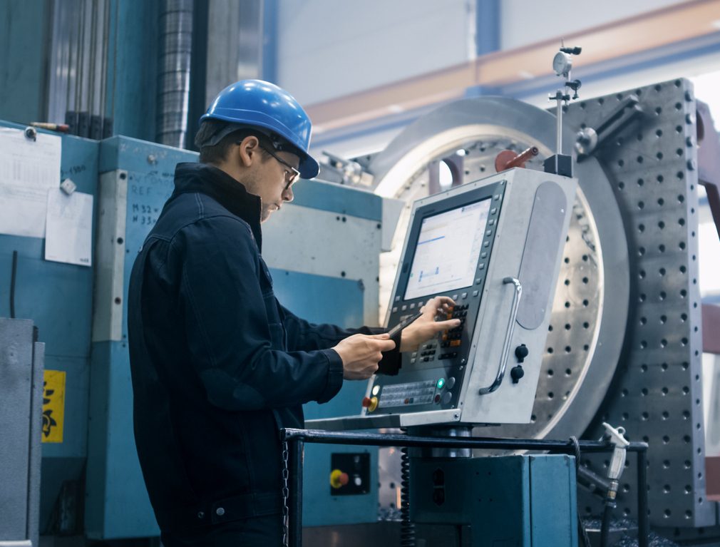 American Micro Industries factory worker programming a CNC milling machine with a tablet computer.