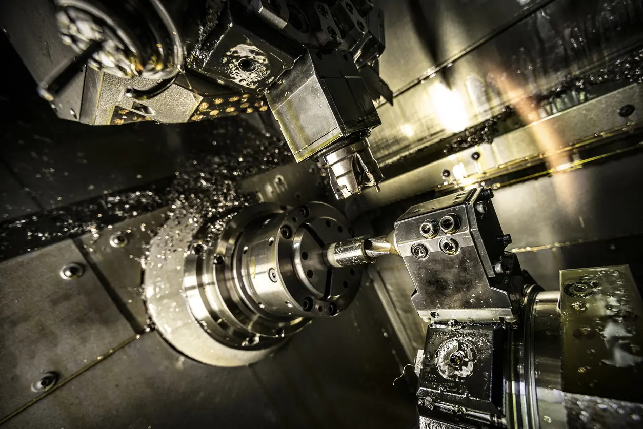 A metalworking tool cuts a workpiece. The machine spins rapidly, producing sparks and coolant spray. The industrial setting is dark and oily.