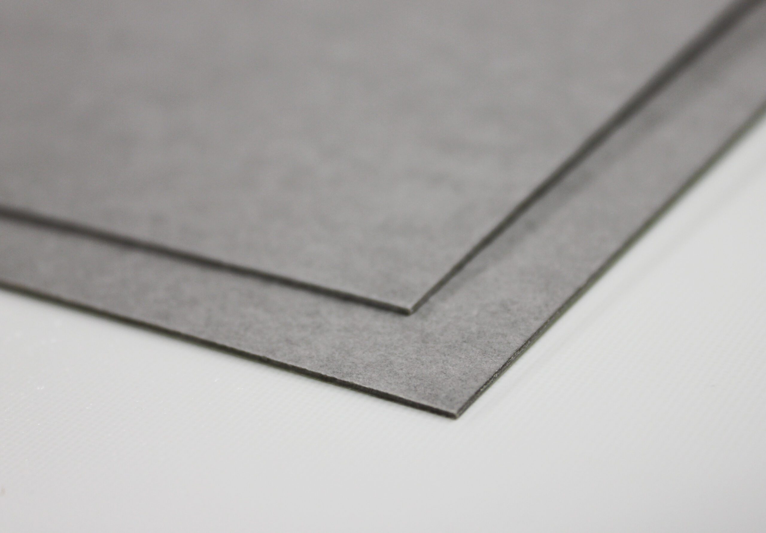 Two gray rectangular sheets of material are stacked, angled on a white surface.