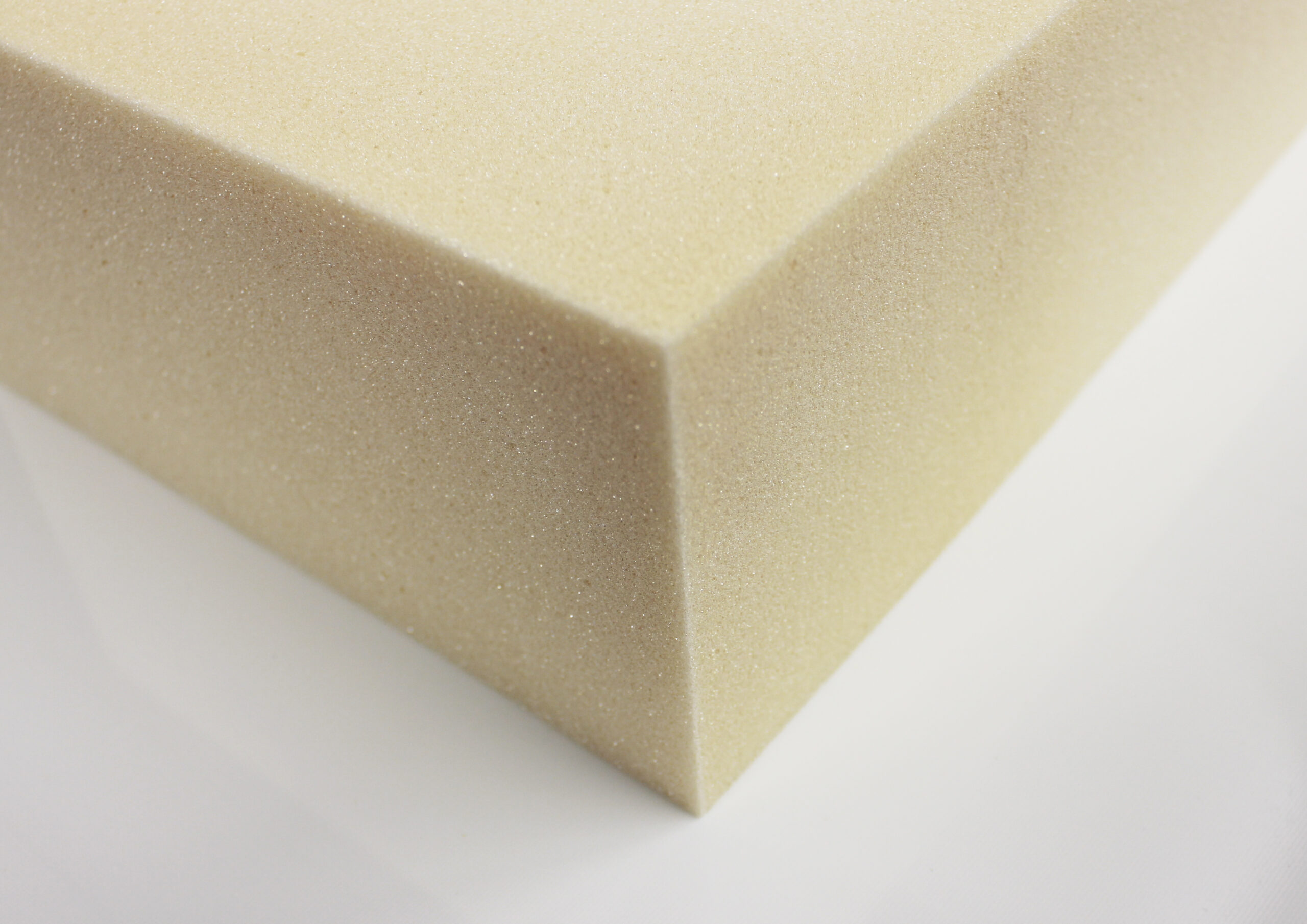 A block of off-white foam rests on a white surface. Its texture is visibly porous.